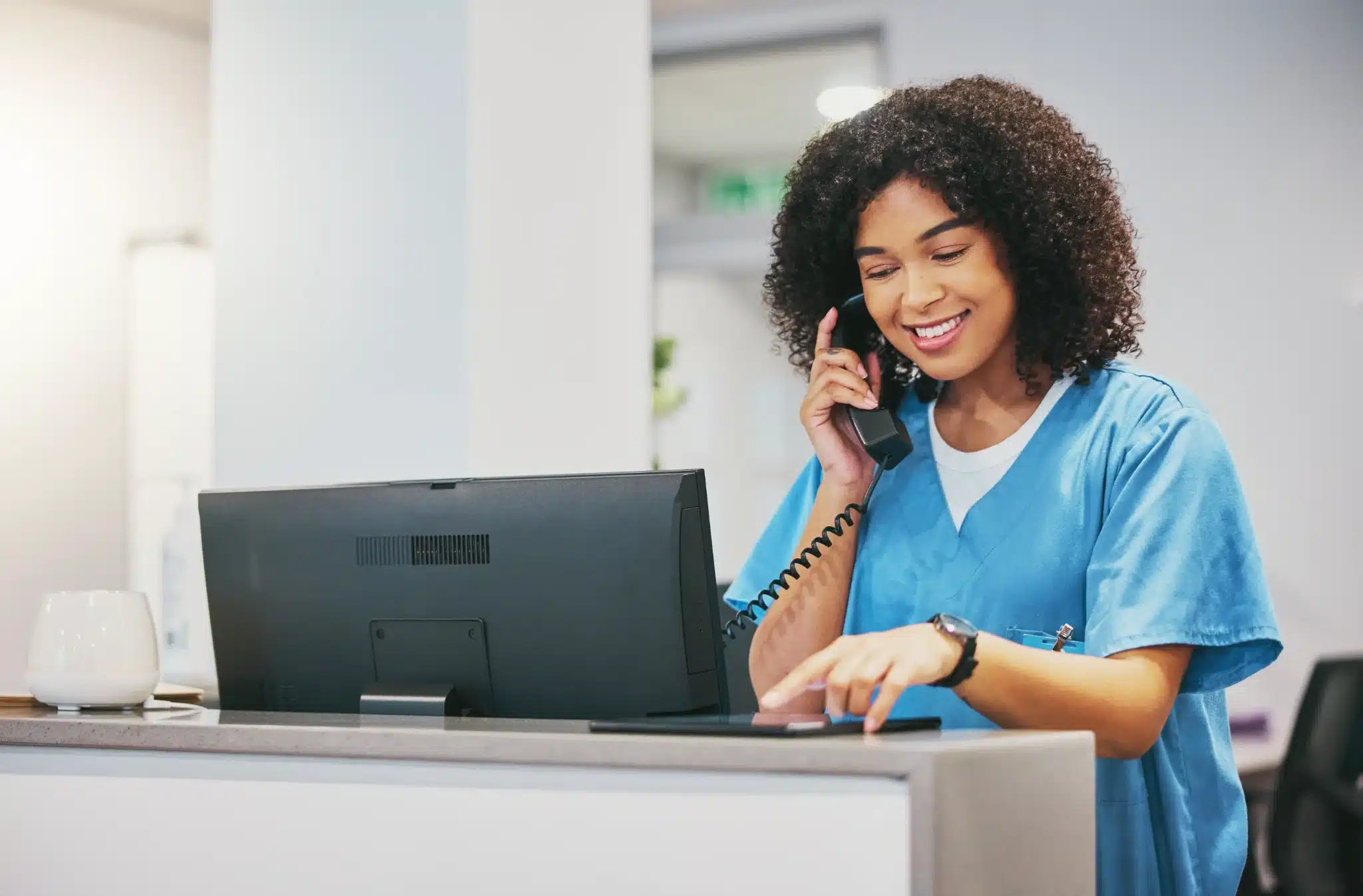 Réceptionniste médicale souriante au téléphone devant un ordinateur dans un cabinet de santé